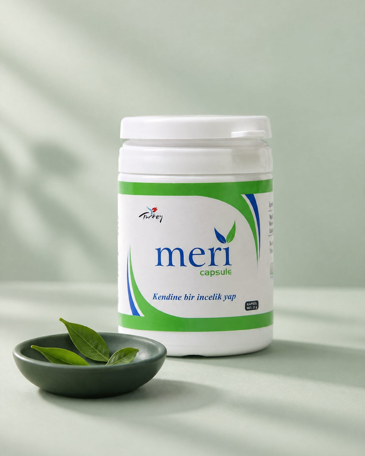 Meri Capsule tub on a sage backdrop with a small green dish of tea leaves in front
